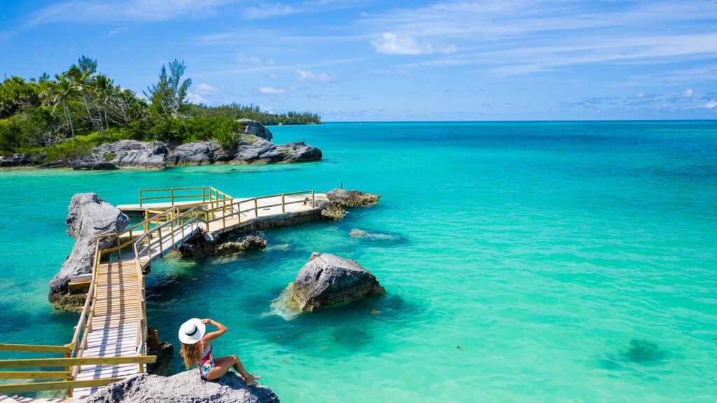 Bermuda ocean with a girl stitting on a rock with a white beach hat