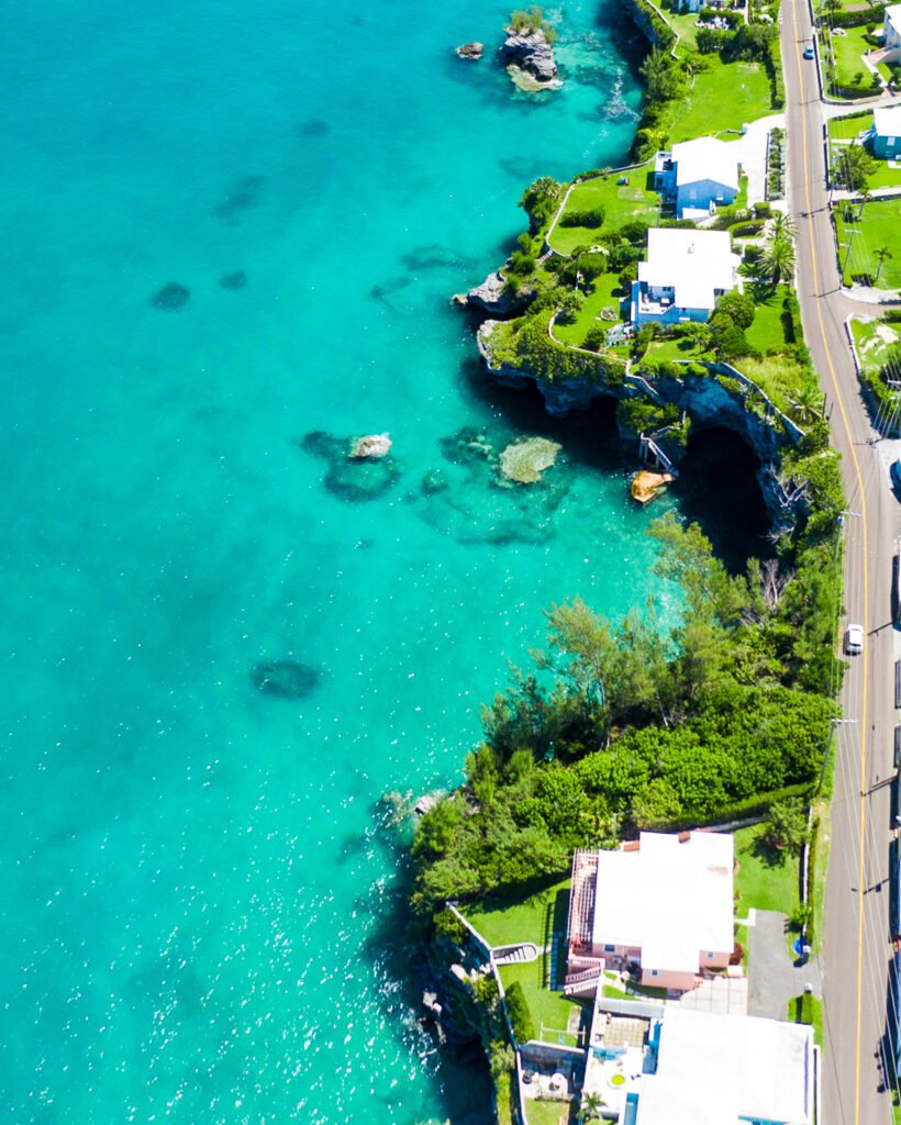 Photo that is vertically almost 50 50 ocean and land with green grass, houses with white roofs and a portion of north shore road